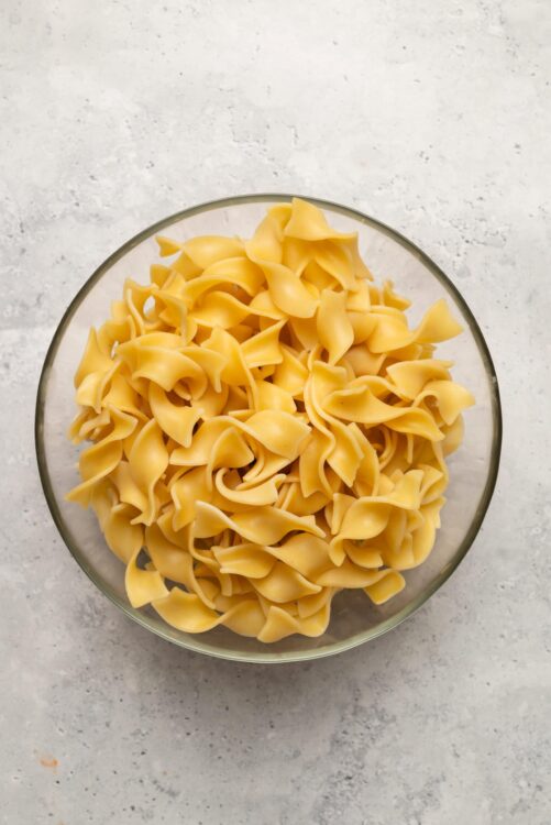 Golden uncooked egg pasta in a glass bowl on white textured surface.