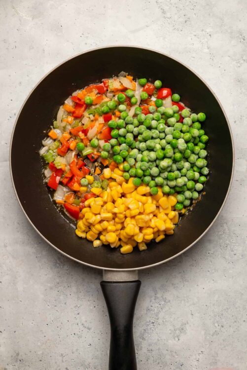 Sautéed colorful vegetables including green peas, corn, red bell peppers, and onions in a skillet.