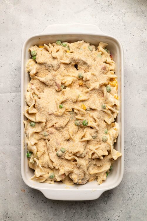 Creamy casserole with peas, ham, and cheesy topping in a white baking dish.