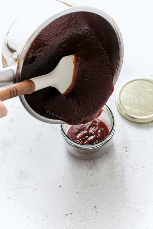 Rich homemade barbecue sauce being poured into a jar, perfect for grilling and cooking recipes.