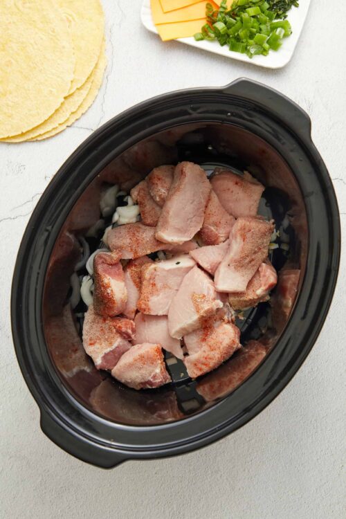 Seasoned raw chicken pieces in a slow cooker for cooking.