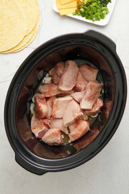 Creamy shredded cheese, fresh green onions, and sliced cheese on a white plate, with tortillas nearby.
