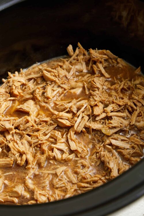 Shredded cooked chicken in a slow cooker with savory broth.