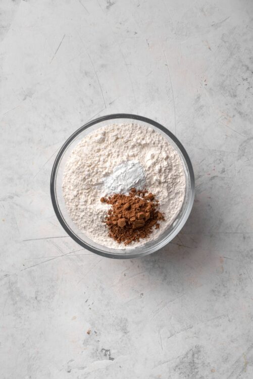 Flour, cocoa powder, and baking soda in a clear bowl for baking recipe.