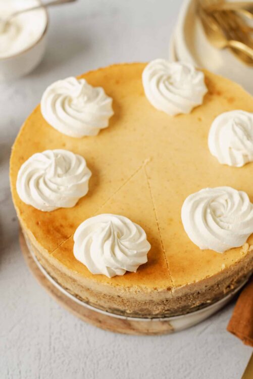 Rich lemon cheesecake topped with whipped cream swirls on a wooden cake stand. Perfect for dessert lovers and special occasions.