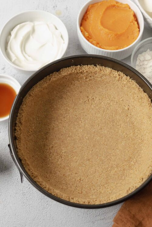 Golden graham cracker crust in a springform pan with dessert ingredients around it.