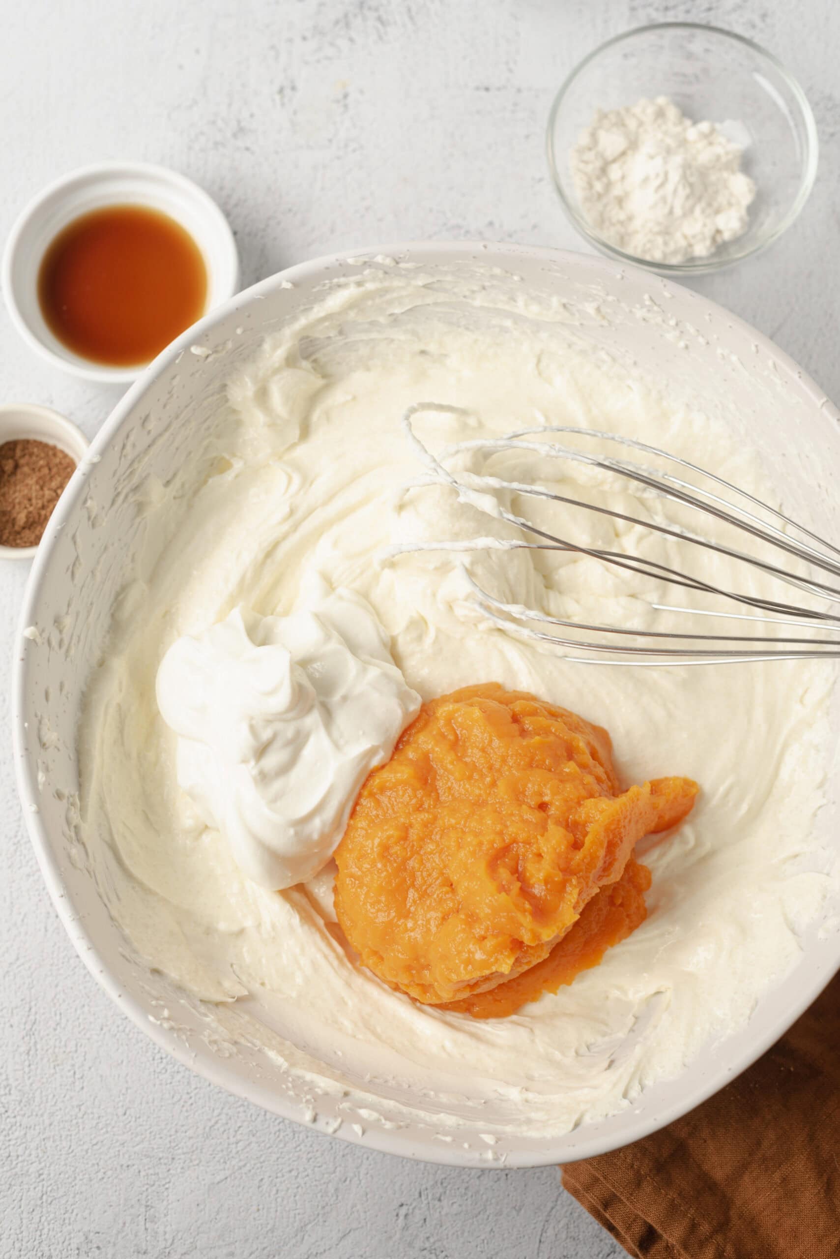 Cream cheese frosting with pumpkin puree and whipped cream in a mixing bowl for baking.