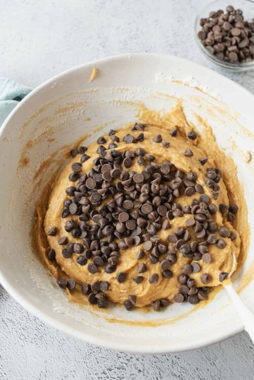 Rich chocolate chip cookie dough in a mixing bowl ready to be baked, with chocolate chips on top.