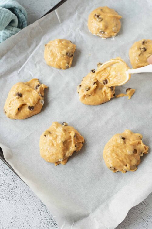 Soft chocolate chip cookie dough balls on parchment paper ready to bake.