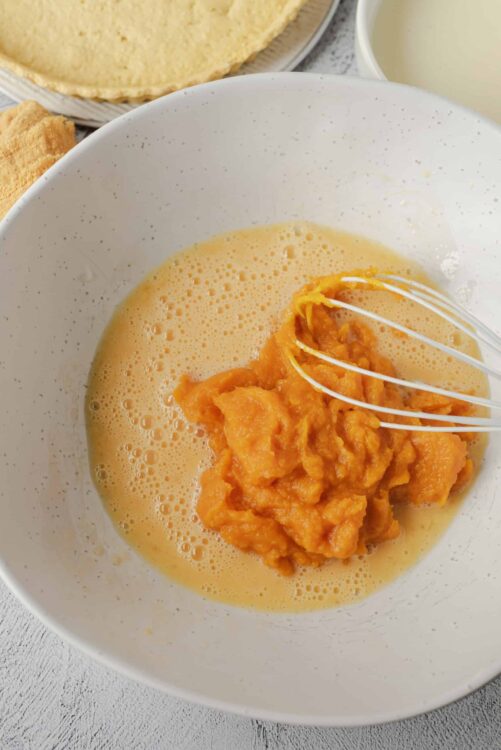 Creamy pumpkin pie filling in a white bowl ready for baking.