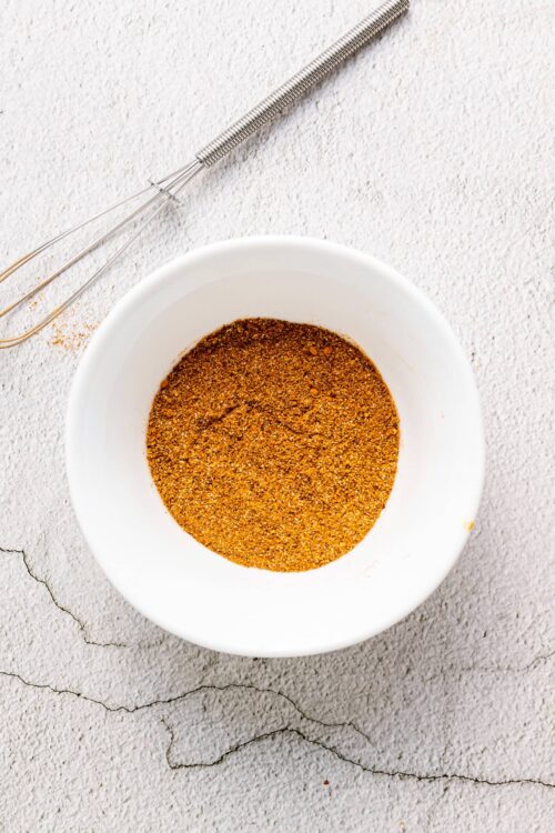 Ground spice blend in a white bowl on textured surface.