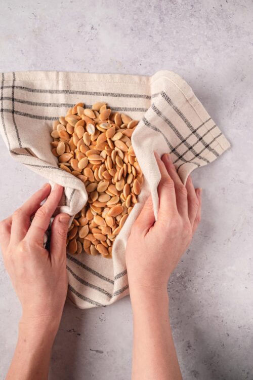 Roasted pumpkin seeds in a cloth bag on a light surface.