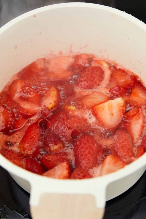Fresh strawberries cooking in a white saucepan for homemade strawberry sauce or jam.