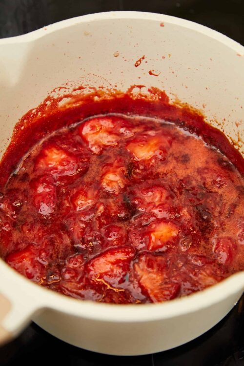 Sweet strawberry jam cooking in a white saucepan, ready for spreading or baking.