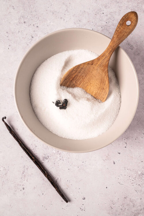 Granulated white sugar with vanilla bean in a white bowl, baking ingredients for desserts.
