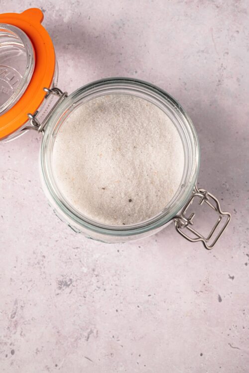 Flour and sugar in a glass jar on a pink textured background.