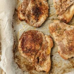 Juicy pan-seared pork chops seasoned with herbs on a baking tray.