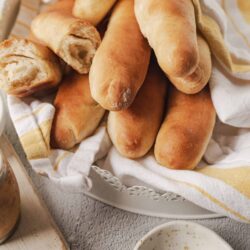 Fluffy homemade bread baguettes in a basket with a white and yellow striped cloth.