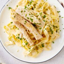 Creamy chicken alfredo pasta with fresh herbs and tender chicken slices on a white plate.