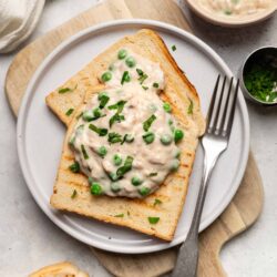 Creamy chicken and pea salad on toasted bread, garnished with chopped herbs.