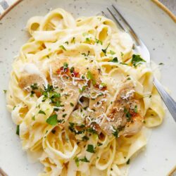 Creamy chicken alfredo pasta with herbs and grated cheese in a white bowl.