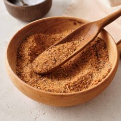 Ground spice blend in a wooden bowl with a wooden spoon, salt in a small bowl behind.