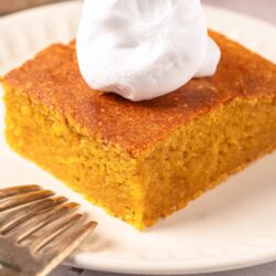 Moist pumpkin bread topped with whipped cream on a white plate.
