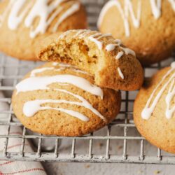 Soft, freshly baked sugar cookies with white icing drizzle on a cooling rack, perfect for holiday treats.