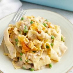 Creamy chicken and vegetable Alfredo pasta served on a white plate with peas and cheese, featuring a delicious homemade sauce.