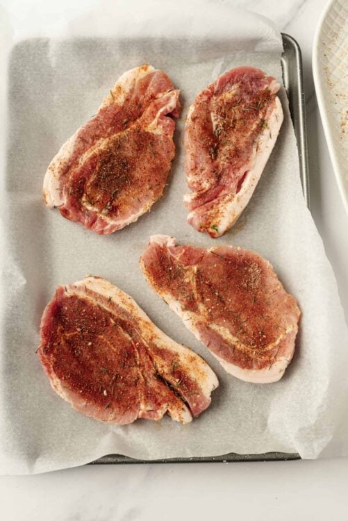 Seasoned raw pork chops on baking sheet for grilling or baking.