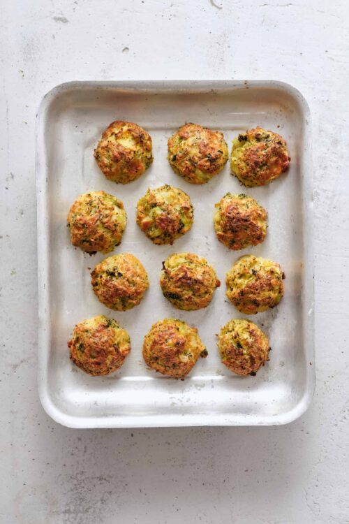 Golden baked broccoli cheese balls on baking sheet, homemade healthy appetizers, crispy snack options.