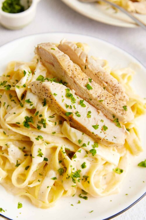 Creamy chicken alfredo pasta with grilled chicken and fresh parsley on a white plate, delicious comfort food.