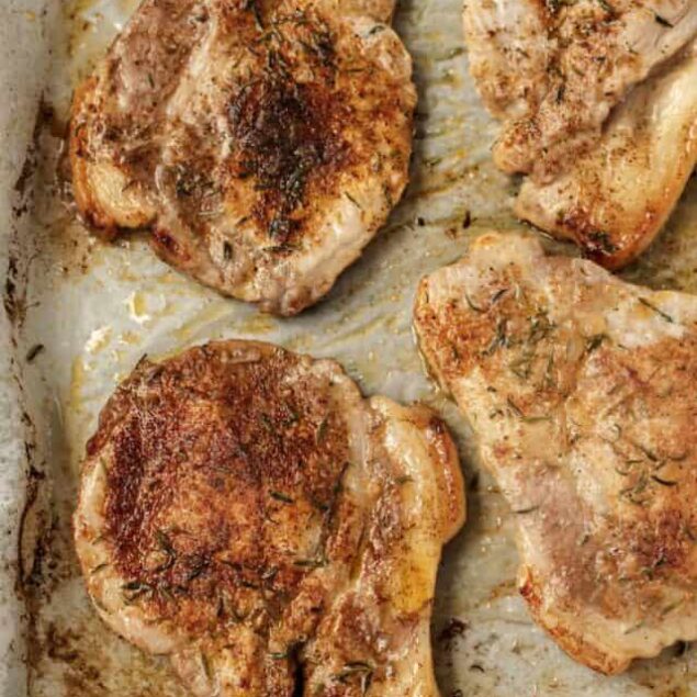 Juicy pan-seared pork chops seasoned with herbs on a baking tray.