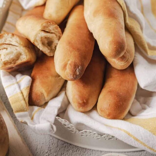 Fluffy homemade bread baguettes in a basket with a white and yellow striped cloth.