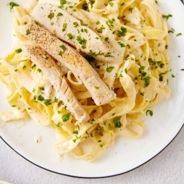Creamy chicken alfredo pasta with fresh herbs and tender chicken slices on a white plate.