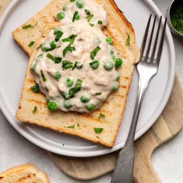 Creamy chicken and pea salad on toasted bread, garnished with chopped herbs.