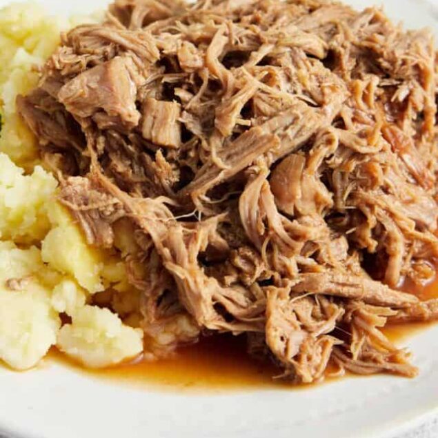 Tender shredded pork with creamy mashed potatoes and fresh herbs on a white plate.
