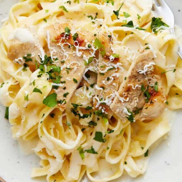 Creamy chicken alfredo pasta with herbs and grated cheese in a white bowl.