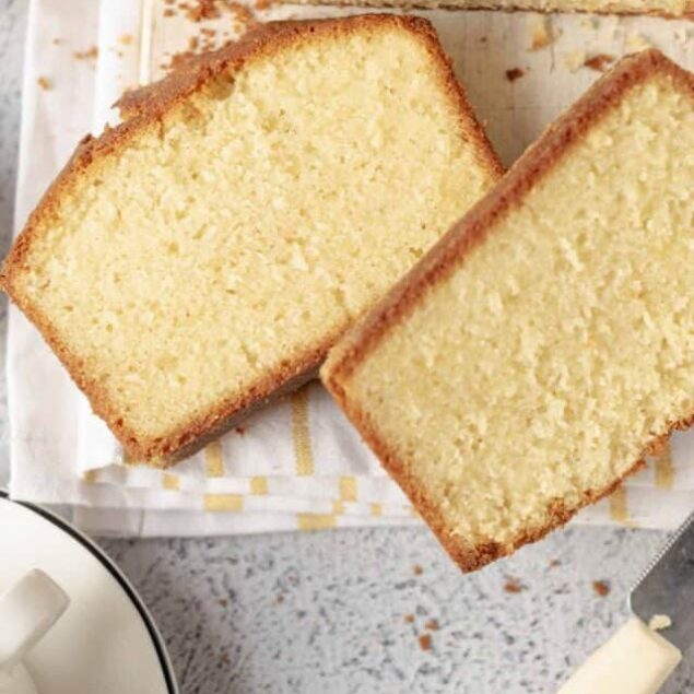 Fluffy homemade vanilla pound cake sliced on a wooden board with a crusty golden exterior.