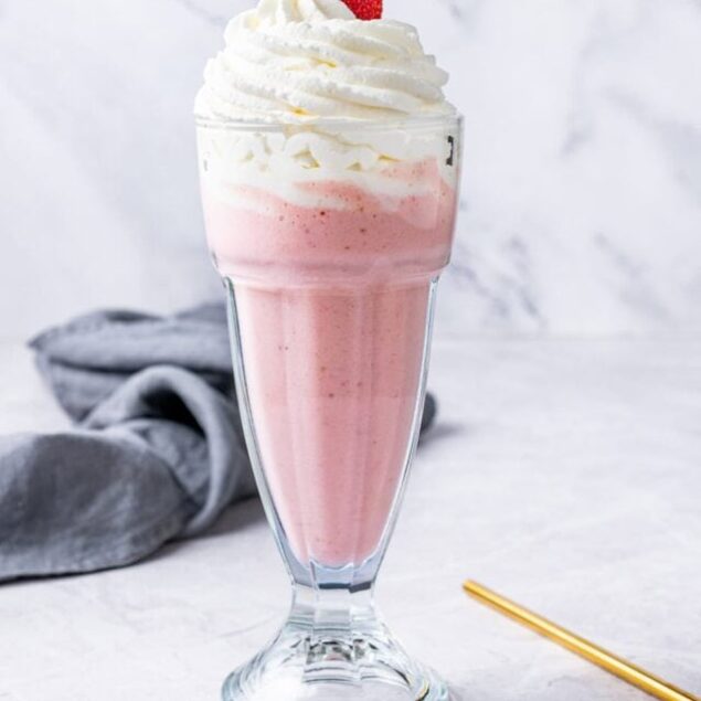 Fresh strawberry milkshake topped with whipped cream and a whole strawberry, served in a tall glass.