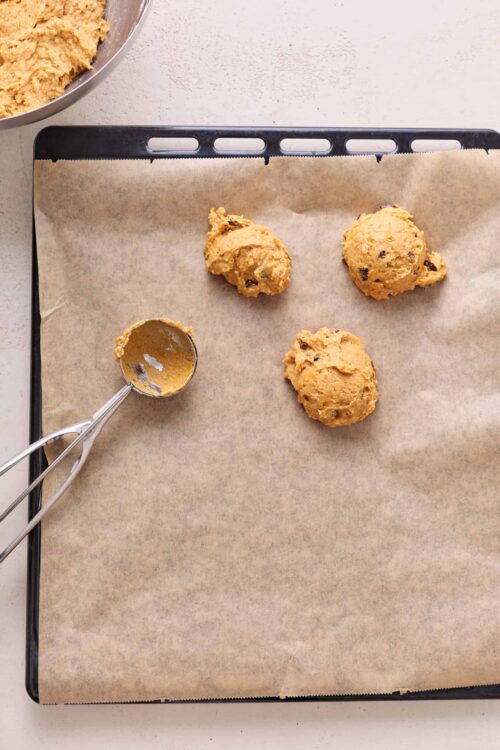Gooey cookie dough balls on parchment paper ready for baking.