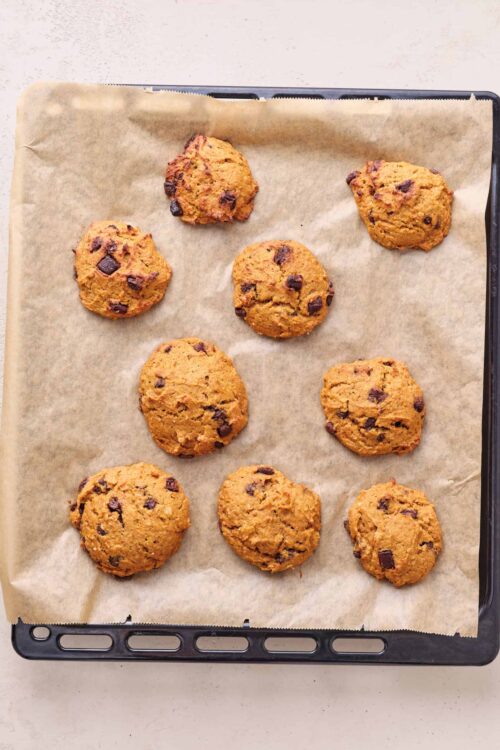 Freshly baked chocolate chip cookies on a baking sheet with parchment paper.