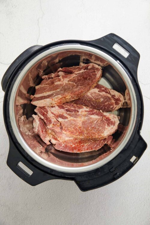 Seasoned raw beef steaks in an instant pot for cooking or slow roasting.