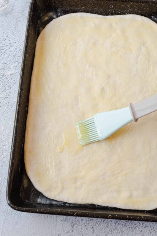 Soft pie crust being brushed with egg wash in a baking pan.