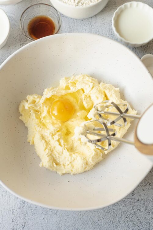 Creamy butter and sugar being mixed with an electric hand mixer in a white bowl for baking.