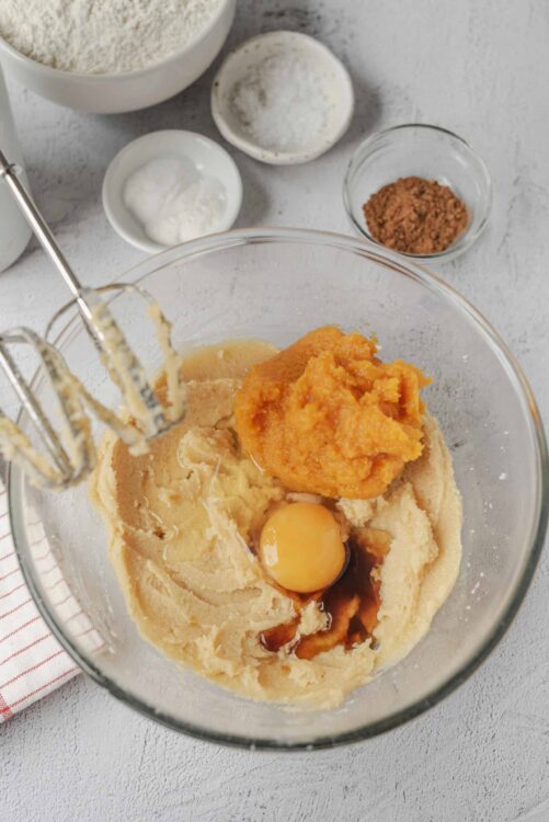 Cream cheese pumpkin bread batter in a glass mixing bowl with baking ingredients around it.