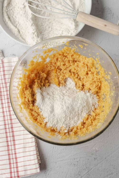 Fluffy orange cake batter mixture with flour in a glass bowl for baking.