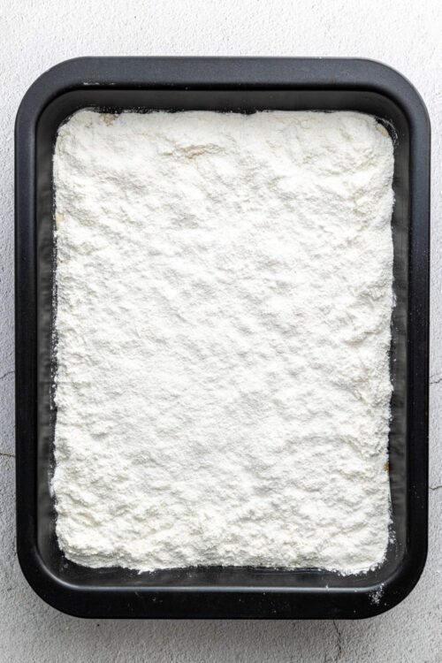 Flour spread in a black baking tray, ready for baking or cooking.
