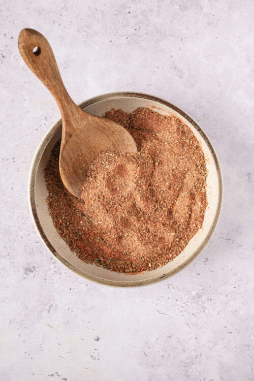 Ground spice blend in a bowl with a wooden spoon, used for baking and cooking.