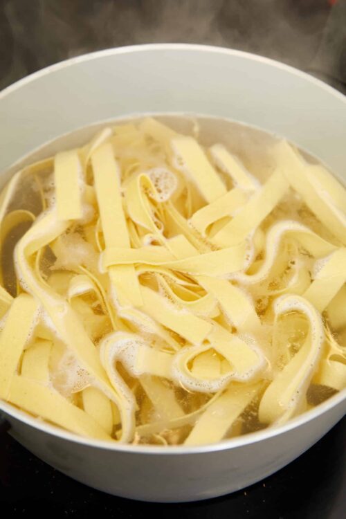 Buttered cooked fettuccine pasta in a white skillet, ready to serve with cheese or sauce.
